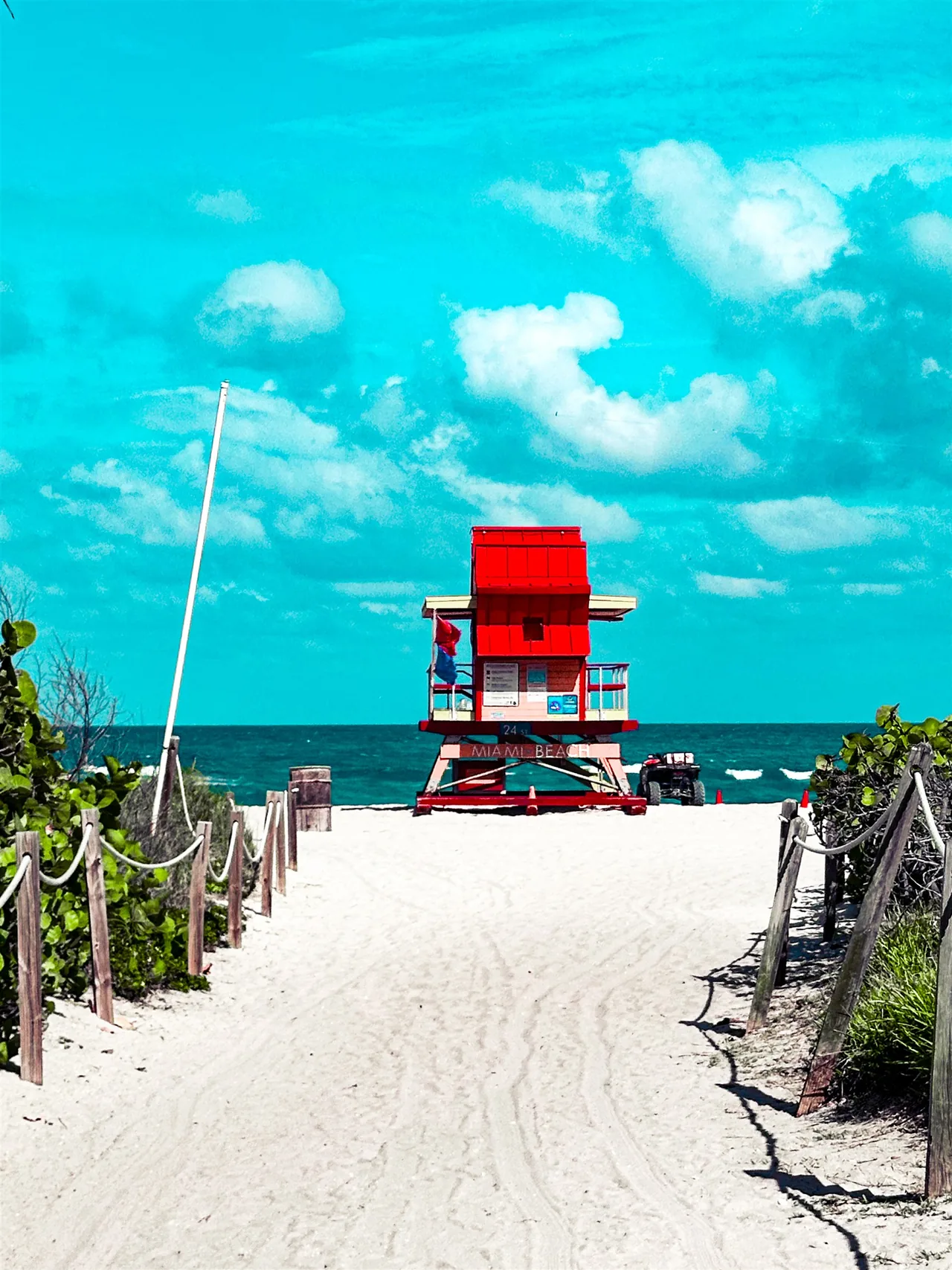 A bright beach path leading toward a red lifeguard tower and the ocean